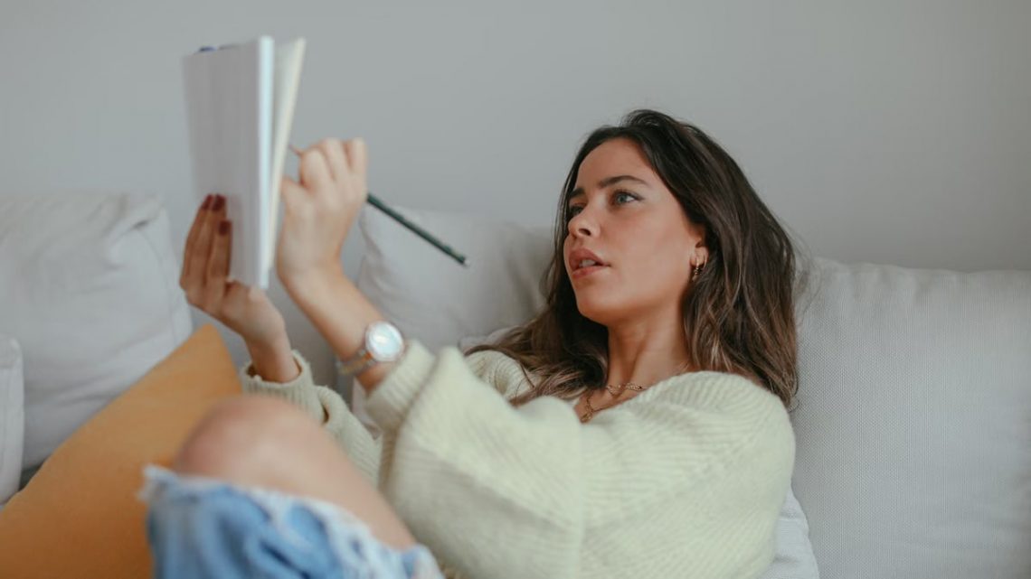 Young woman relaxing on couch while writing in notebook indoors.